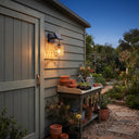 PT0909 solar wall light on grey shed exterior at twilight, illuminating potting bench with seedlings and gardening tools — practical outdoor task lighting with rustic charm and dual solar/USB power.