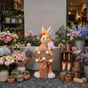 Decorative rabbit statue with 'Welcome' sign surrounded by flowers and gardening tools.