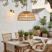 Outdoor dining area with wooden table, chairs, and potted plants under a hanging rattan light fixture.