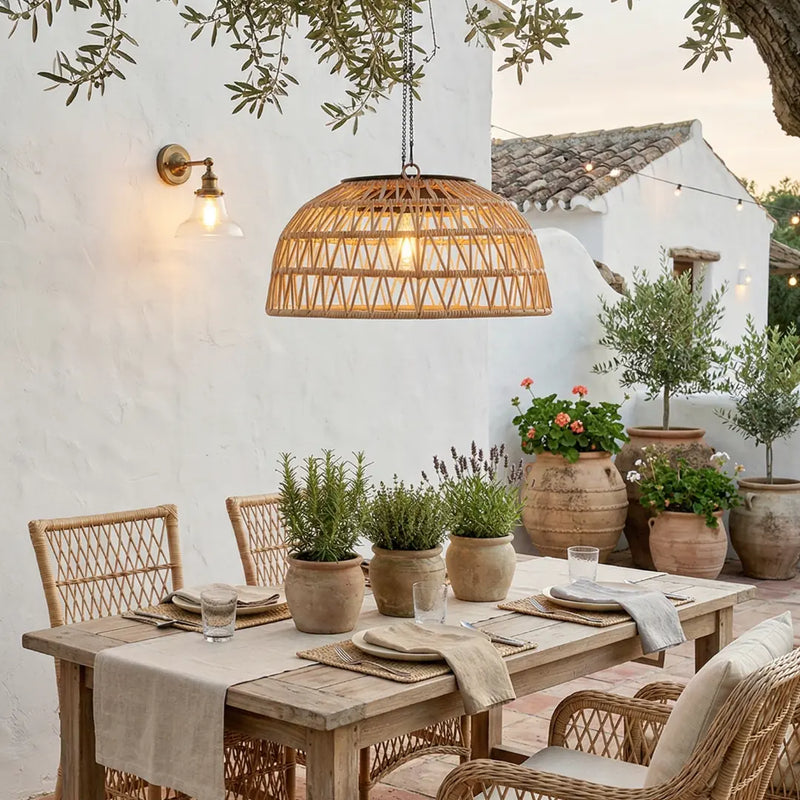 Outdoor dining area with wooden table, chairs, and potted plants under a hanging rattan light fixture.