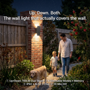 Family walking with a dog near a wall light in a garden setting