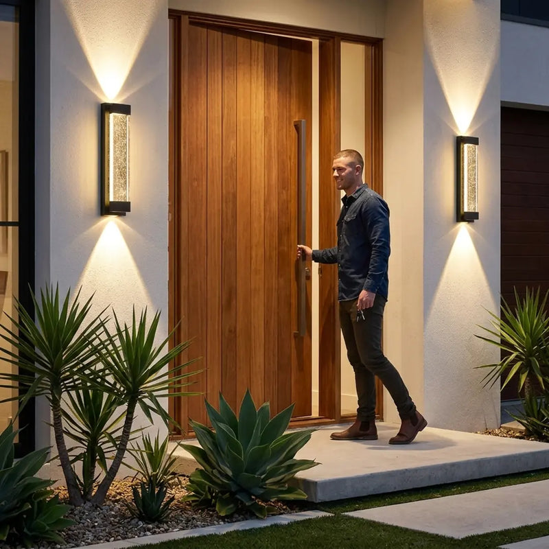 Man opening a wooden door with modern outdoor lighting and plants.