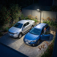 T008 solar street light mounted on a driveway fence lighting up a parked car and garage area, highlighting the IP65 waterproof rating and reliable outdoor security lighting for homes.