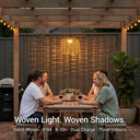 Group of friends enjoying wine at an outdoor table under a wooden pergola, illuminated by a handwoven rattan solar pendant light; text overlay reads "Woven Light. Woven Shadows." with features: Hand-Woven, IP44, 8-10H runtime, Dual Charge, Three colours.