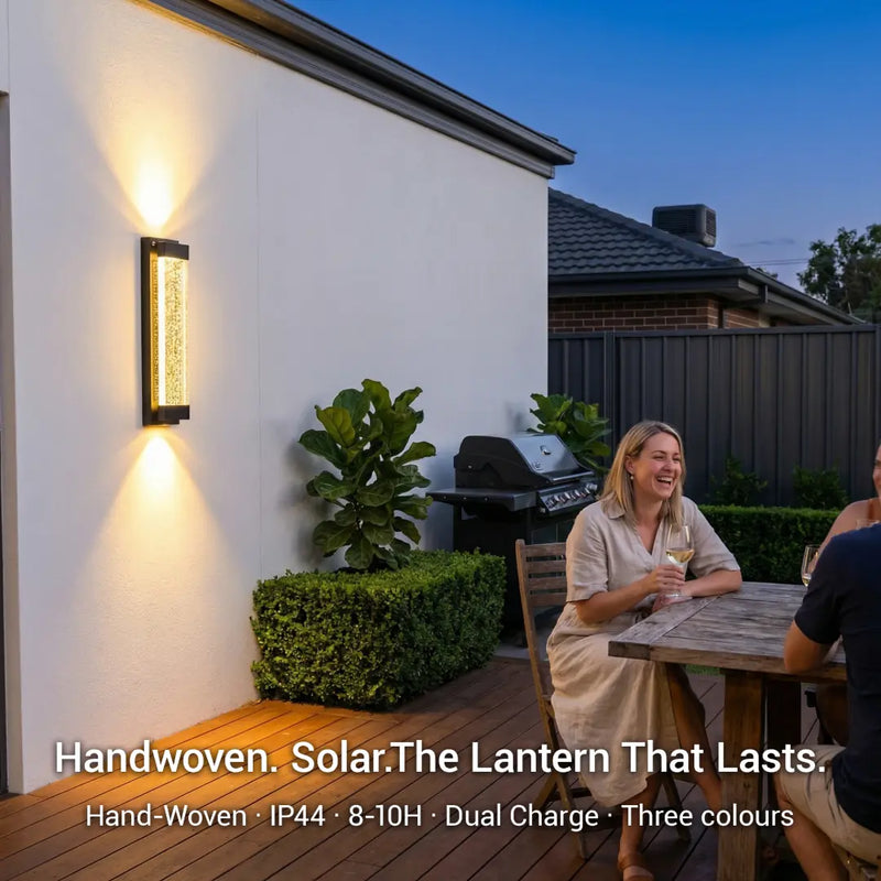 Two people sitting at a table outside a house with a solar lantern on the wall.