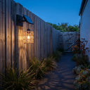 PT0909 solar wall light mounted on weathered timber fence along garden pathway at dusk, casting soft glow over ornamental grasses and succulents — serene evening ambiance with handwoven PE rattan texture.