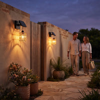 Couple walking past two PT0909 solar wall lights on stone-paved garden path at twilight; warm woven shadows illuminate brick and stucco walls — romantic, maintenance-free outdoor lighting for evening strolls.