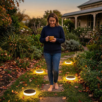 Woman walking barefoot on a garden path lined with illuminated Niteo solar lights at dusk, showcasing the lights guiding the way along a stone walkway surrounded by autumn foliage.v