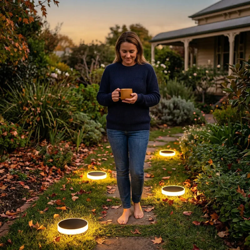 Woman walking barefoot on a garden path lined with illuminated Niteo solar lights at dusk, showcasing the lights guiding the way along a stone walkway surrounded by autumn foliage.v
