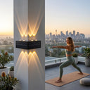 A woman practicing yoga in a warrior pose on a high-rise balcony at sunrise, with the Grivo solar corner light mounted on a pillar casting warm up and down lighting, set against a backdrop of the Sydney city skyline.
