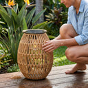 Woman touching PT0906 solar handwoven lantern on wooden deck, PE rattan texture, garden lighting close-up, tropical plants background