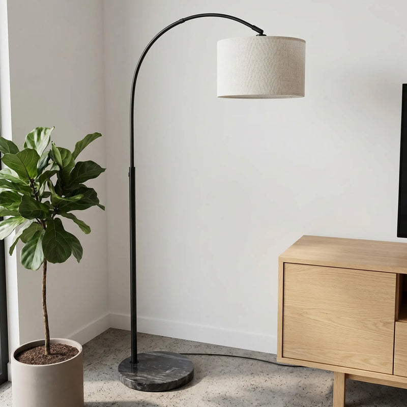 Arc floor lamp with a white shade in a room with a plant and wooden cabinet.
