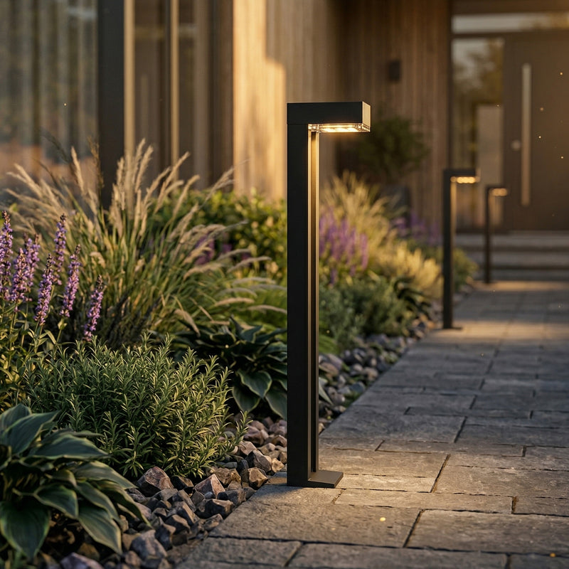 Garden pathway with a modern outdoor light fixture, surrounded by plants and rocks.