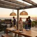 Two PT0901 Kiku Solar Rattan Lanterns illuminating an outdoor deck during a sunset BBQ party, providing warm ambient light for dining and socializing with a city skyline view.