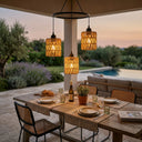 Outdoor dining setup with wooden table, chairs, and hanging lantern lights in a garden setting.