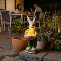 Decorative rabbit light with a glowing ball on a patio with potted plants and people in the background.