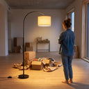 Woman standing in a room with unpacked boxes and a floor lamp.