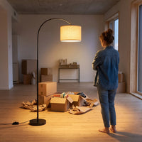 Woman standing in a room with unpacked boxes and a floor lamp.