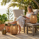 Woman reading book on coastal patio with PT0906 solar rattan lamps, ocean view, boho outdoor decor, warm 3000K lighting
