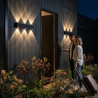 
Couple arriving home at night welcomed by two solar wall wash lights flanking dark timber front door with warm 3000K diamond light pattern and Australian native garden
