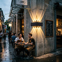 Two baristas taking a break at an outdoor table in front of a cafe, illuminated by the Grivo solar corner light mounted on a commercial concrete brick corner, highlighting its suitability for hospitality and business exterior lighting.