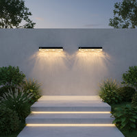 Two outdoor wall lights illuminating a set of steps with plants on either side.