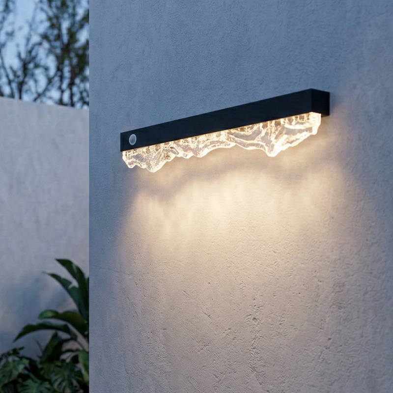 Modern outdoor wall light fixture on a textured white wall with a plant in the corner.