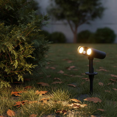 turned on solar spotlight , casting light on the grass near a tree, highlighting the area in a serene environment.
