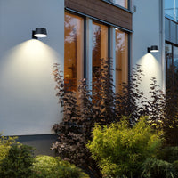 Modern building exterior with wall-mounted lights illuminating plants at night.