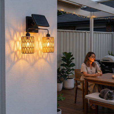 Kasa Duo PT0910 solar wall light with two PE rattan lanterns on one bracket, casting layered shadows on white stucco wall — ideal for patio or entryway ambiance with warm 3000K glow and IP54 weatherproof design.