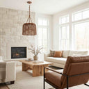 A warm, modern living room featuring a brown leather accent chair in the foreground, a white sofa, a light wood coffee table, and a large woven wicker pendant light hanging over a fireplace built into a white stone wall.