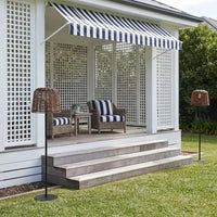 Wicker solar floor lamp on grassy patio with striped awning and outdoor seating.