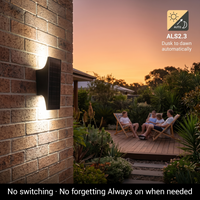 Outdoor wall light fixture on a brick wall with people sitting on a deck at dusk.