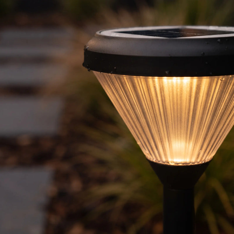 Close-up of diamond-cut prism lens glowing warmly, water droplets on black aluminum housing highlight IP65 weatherproof design.