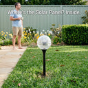 Close-up of a solar globe light on a lawn showing the hidden internal solar panel design with a man in the background.