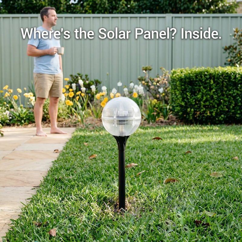 Close-up of a solar globe light on a lawn showing the hidden internal solar panel design with a man in the background.