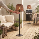 Hand adjusting lamp height on covered patio — illustrates freestanding mobility, paired with BBQ area and dining setup, emphasizing no-drill installation and renter-friendly design.