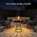 Outdoor lounge setup with fire pit, chairs, and table at night.