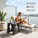 Woman playing guitar on a balcony with a plant and table in the foreground, and cityscape in the background.