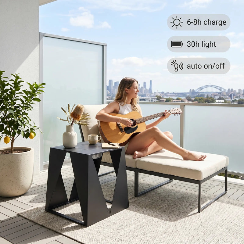 Woman playing guitar on a balcony with a plant and table in the foreground, and cityscape in the background.