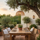 Outdoor dining setup under a large tree with a wooden table and wicker chairs.