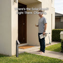 A man holding a coffee and newspaper stands barefoot at his front door beside a Rivix PT0723 solar bollard charging in daylight, with overlay text reading "Where's the Solar Panel? Right There. Charging."