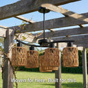 Woven outdoor light fixtures hanging from a wooden pergola with a garden background.