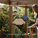 A woman stands on a wooden step stool under a pergola in a garden, holding a small solar panel next to a hanging woven basket-style outdoor lamp. Text on the image says, 'Replace the Solar Panel.