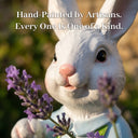Close-up of a hand-painted white resin rabbit garden ornament with a pink nose, surrounded by purple lavender flowers, with text overlay reading Hand-Painted by Artisans Every One Is One of a Kind