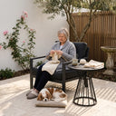 Woman knitting outdoors with a dog lying on the ground next to her.
