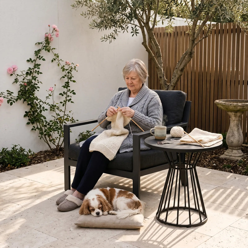 Woman knitting outdoors with a dog lying on the ground next to her.