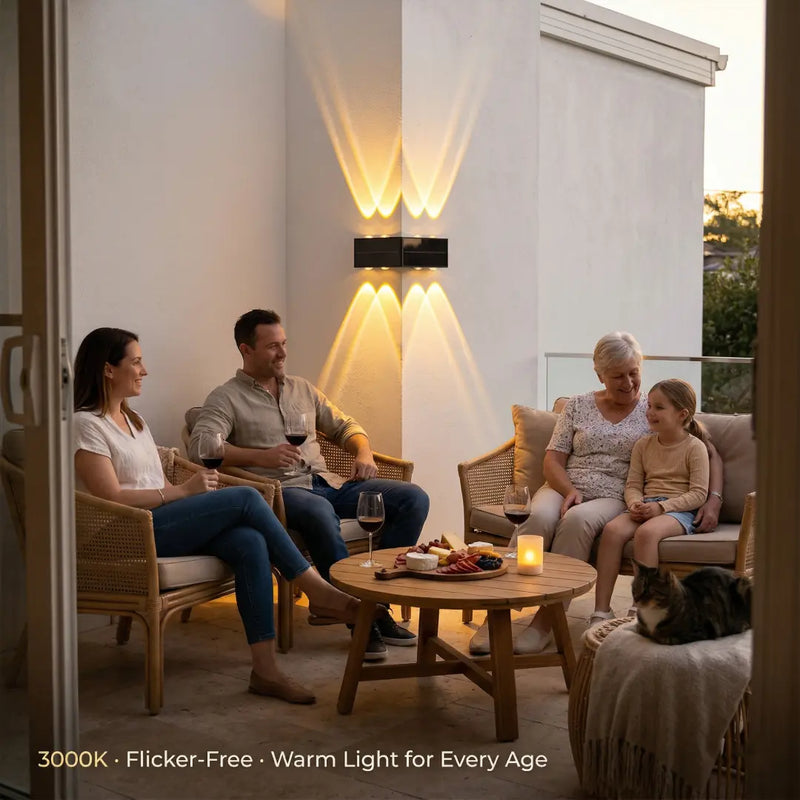 A family of four enjoying dinner on an outdoor deck, with the PT0803 Grivo solar corner light providing warm, ambient illumination on the white wall behind them. The text '3000K · Flicker-Free · Warm Light for Every Age' emphasizes its eye-friendly, anti-glare design perfect for family gatherings.