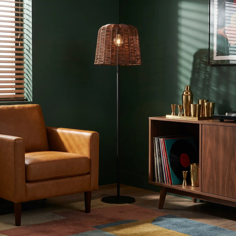 Indoor wicker floor lamp next to leather armchair and wooden media console.
