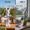 Split image showing a white resin rabbit garden ornament outdoors on a sunny day charging via solar on the left, and the same ornament indoors on a rainy day plugged in via USB-C cable on the right, with text overlay Dual Charge Never Dark